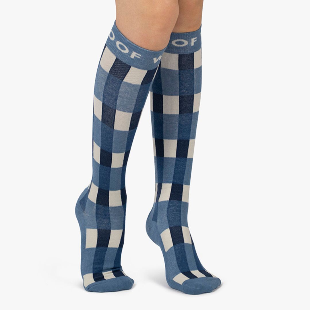 Nurse wearing blue and white gingham plaid knee-high compression socks with top cuff branding.