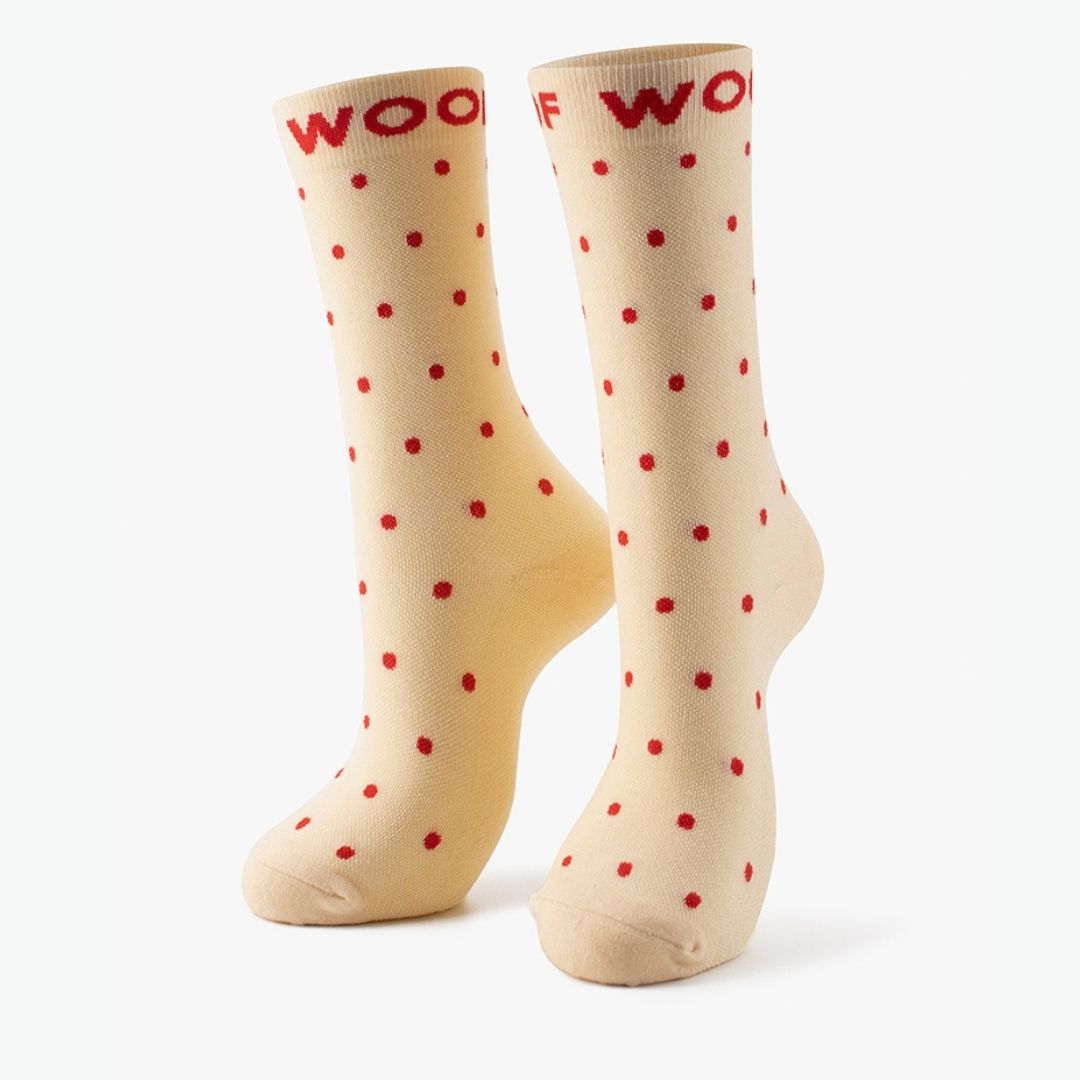 A pair of cream Polka Dots Bamboo Crew Compression Socks standing upright, featuring red polka dot motifs with bold red "WOOF" woven into the top cuffs.  