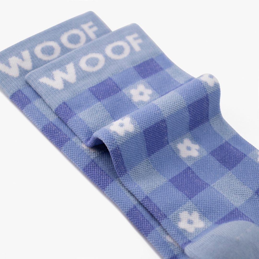 A Floral Gingham Bamboo Crew Compression Socks folded neatly to highlight the light blue woven "WOOF" cuff bands and the floral gingham knit pattern layout.  