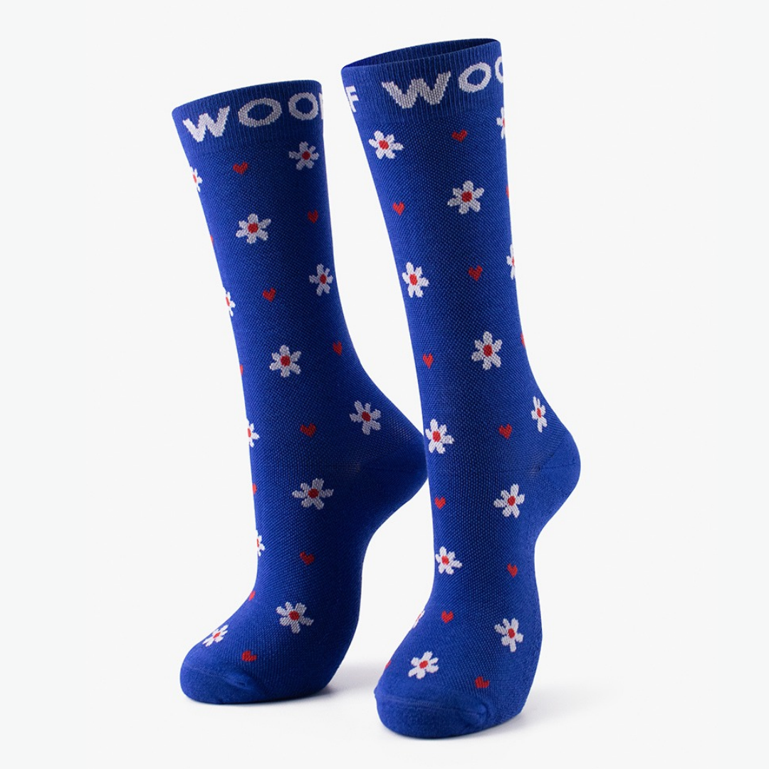 Daisy & Heart Bamboo Crew Compression Socks standing upright, featuring a cheerful repeating pattern of white daisy flowers with red centers alongside tiny red hearts, finished with a matching royal blue woven "WOOF" top cuff.