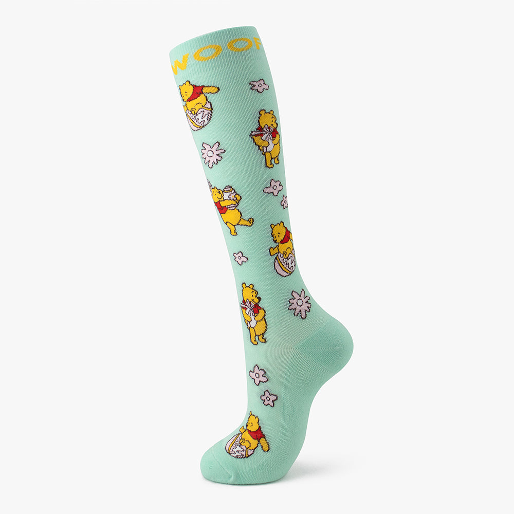 Studio shot of the mint green pair from the Disney’s Winnie the Pooh Bamboo Compression Socks 6 Pack, highlighting a yellow "WOOF" cuff band and Winnie the Pooh floating with honey bees.   